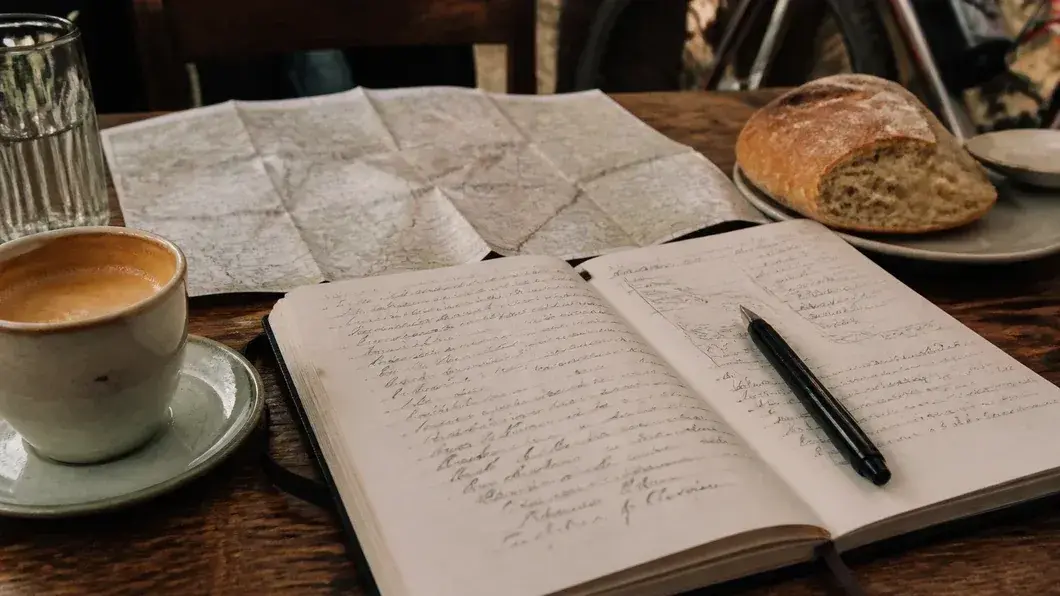 Un carnet ouvert à côté d'un petit pain local et d'une carte de randonnée sur une table de café